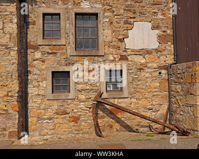 2 large old ships anchors by a stone wall with 4 irregular windows and a white space where another window was blocked up in Anstruther, Scotland,UK Stock Photo