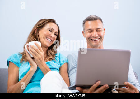 Happy Mature Couple Sitting On Sofa Watching Movie In Laptop At Home Stock Photo