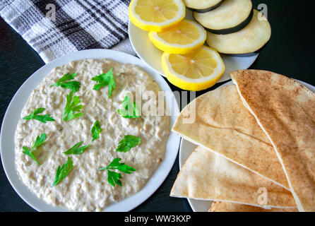 Famous traditional Arabic cuisine - dip Baba ganoush with pita bread and fresh lemon on dark wooden table. Flat lay, top view. Baba ganoush. Stock Photo