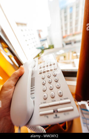 Man hand holding old vintage keypad telephone in hand in hotel room - focus on the phone's keypad Stock Photo