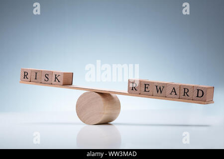 Close-up Of A Wooden Seesaw Showing Imbalance Between Risk And Reward On Reflective Background Stock Photo
