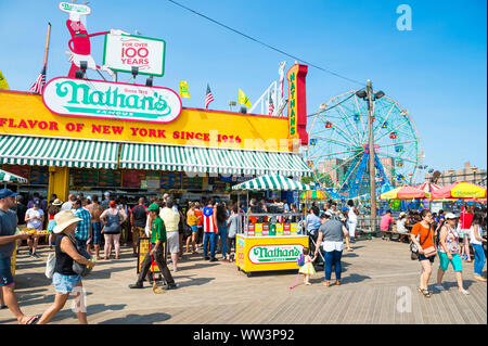 NEW YORK CITY - AUGUST 20, 2017: Visitors walk the iconic wooden Coney Island boardwalk outside the famous Nathan's hot dog stand on a hot summer day. Stock Photo