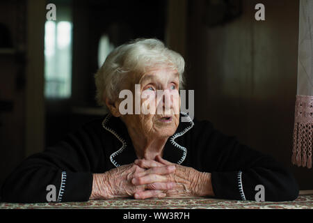 Elderly old woman looks sadly out the window. Care for lonely pensioners. Stock Photo