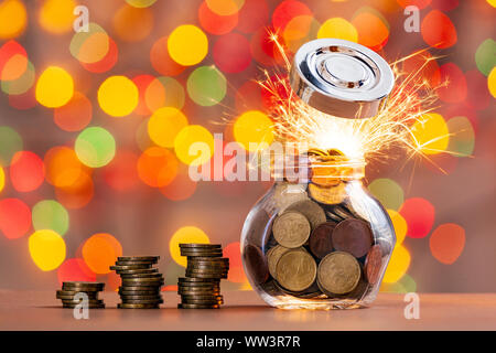 Rows of coins and a jar of coins on a table with shiny background. Bright rays of light from under the flying cover. The concept of saving money. Stock Photo