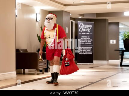 Montreal, Canada. Jul 2019. Man in a Santa costume exposing some hard body workout abs leaving a booze bar after an Happy Hour event.
