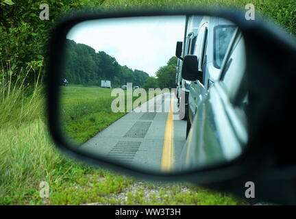 Car side mirror view of sleeper lines or rumble strips on road shoulders are there to wake up or alert sleepy or drunk drivers. Stock Photo