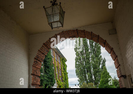 Red brick arch entrance into victorian style building with green trees in background. Stock Photo
