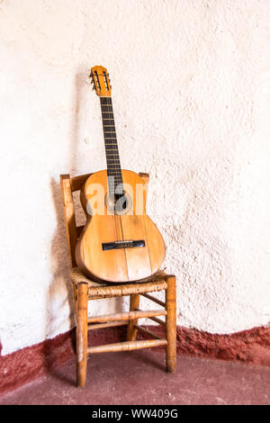 A classical, acoustic guitar laying on a chair and leaning against a white wall. Stock Photo