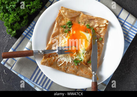Breton crepe, Savory Buckwheat Galettes Bretonnes with spilled egg, cheese, ham on a white plate on a concrete table, horizontal view from above Stock Photo
