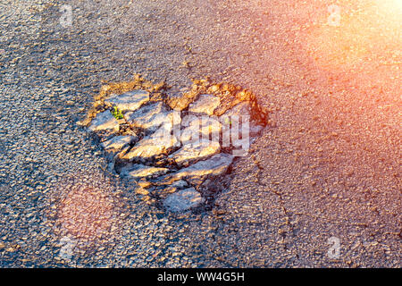 potholes on the asphalt the shape of a heart in the rays of the sun. Texture background Stock Photo