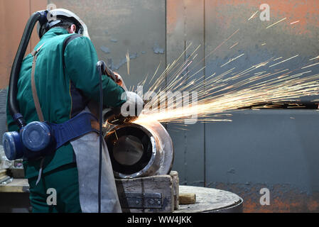 worker machined workpiece casting with a grinding machine - work safety with protective clothing Stock Photo