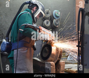 worker machined workpiece casting with a grinding machine - work safety with protective clothing Stock Photo