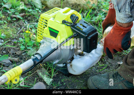 Farmer adding petrol gas to the gasoline tank of the trimmer brushcutter in the field. Technology. Stock Photo