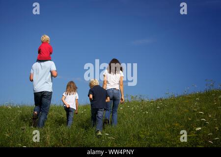 Family walking in meadow, view from behind. Stock Photo