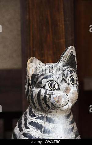 Gotoku ji Temple, Tokyo, Japan.  The carved wood figure of actual  likeness of Maneki Neko, also known as a Lucky Cat sits by the temple building. Stock Photo