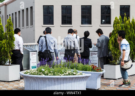 Ueno station, Tokyo, Japan.  Japanese businessman smoking at a public smoking area off Ueno station , all facing the same direction while they smoke. Stock Photo
