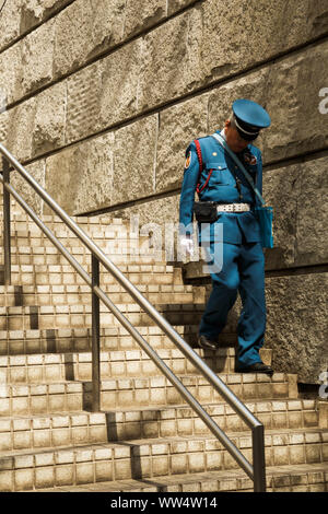 A tired looking Japanese male security guard who is also a senior citizen, going down the stairs outside his work place in Shinjuku, Tokyo, Japan. Stock Photo