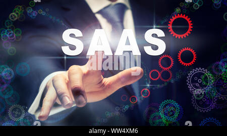 A businessman pressing a SaaS business concept on a graphical display of cogs Stock Photo