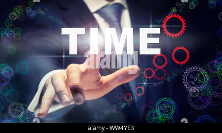 A businessman pressing a Time business concept on a graphical display of cogs Stock Photo