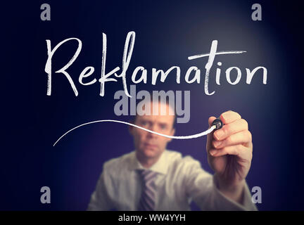 A businessman writing a Claim "Reklamation" concept in German with a white pen on a clear screen. Stock Photo