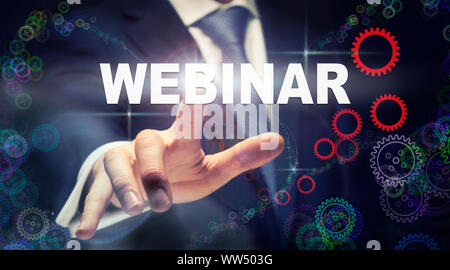 A businessman pressing a Webinar business concept on a graphical display of cogs Stock Photo
