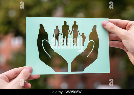 Hands Holding Paper With Cutout Hands Protecting Family Outdoors Stock Photo