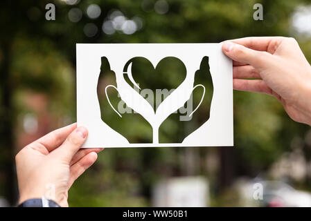 Hands Holding Paper With Cutout Hands Protecting Heart Outdoors Stock Photo