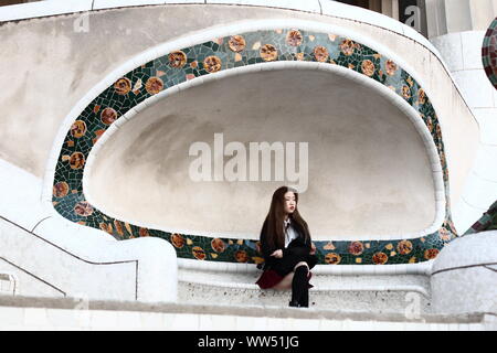 A young Asian woman sitting alone on a bench in the Park Guell in Barcelona, Stock Photo