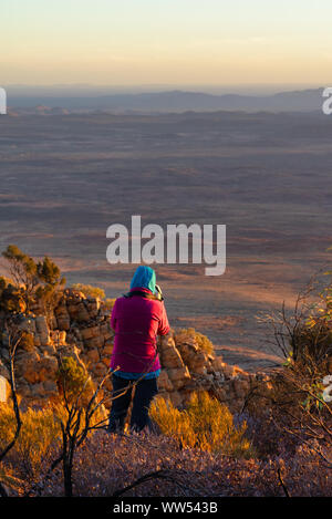 Woman standing on Mt Sonder taking a photo at sunrise, West MacDonnell National Park, Northern Territory, Australia Stock Photo