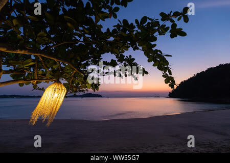 Tillandsia lamp hanging at the tree and swinging under the wind on a tropical beach at dusk, Thailand Stock Photo