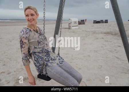 Half portrait woman on the beach sitting on swing with beach chairs and sea in the background Stock Photo