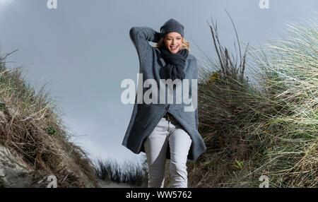 Laughing woman with cardigan and cap going for a walk in the dunes Stock Photo