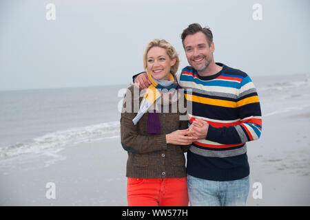 Half portrait of a couple embracing and going for a walk on the beach Stock Photo