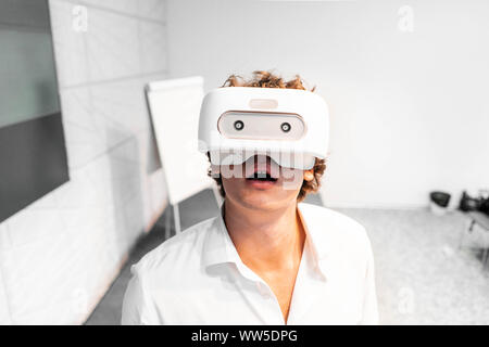 Amused and shocked Man wearing virtual reality goggles in modern contemporary bright co-working office. the VR experience. Stock Photo
