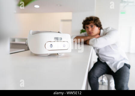 Man sitting near virtual reality goggles in modern contemporary bright co-working office. the VR experience. Man is on background and blurred, Stock Photo
