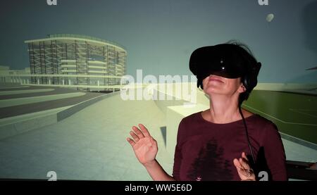 Halle, Germany. 13th Sep, 2019. A woman wearing virtual reality glasses stands in front of a screen in an exhibition room in the Volkspark, showing a virtual tour of the "Stadtkrone" area on the banks of the river Saale. Around 1920 an architectural competition took place in which Walter Gropius took part and designed a city centre. From 14.09.2019 to 19.01.2020, visitors can experience the urban design of the Bauhaus founder in a show by the Volksparkverein and the Burg Giebichenstein Kunsthochschule Halle. Credit: Sebastian Willnow/dpa-Zentralbild/ZB/dpa/17�Թ����� Live News Stock Photo