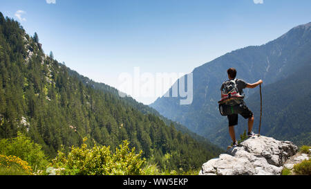 30-40 years old man with backpack standing on rock ledge looking in the valley Stock Photo