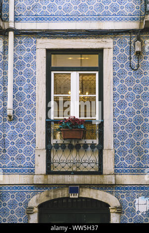 vertical photo of a typical historic vintage house balcony with flowers in an old tile facade with geometric pattern, picturesque architecture at Lisb Stock Photo