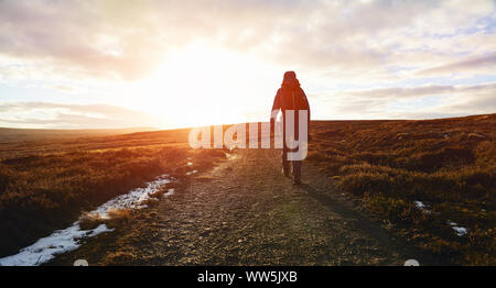 A hiker walking along a narrow dirt track over the moors near Edmundbyers at sunset. Stock Photo