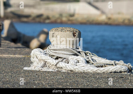 Concrete mooring bollard with a rope around it at a dock. Stock Photo