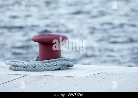 Concrete red mooring bollard with a rope around it at a dock. Stock Photo
