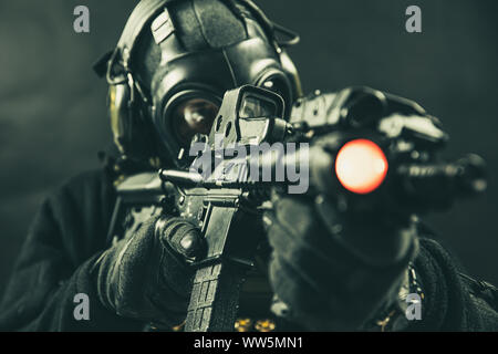Elite special unit soldier with gasmask is holding assault rifle and aiming at the target Stock Photo