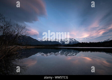 Reflection of the western Karwendel Mountains in the Barmsee. From left dramatic clouds coming up, the Alps slightly snowy. Stock Photo