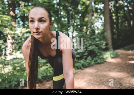 Sporty female preparing to run in the forest. Young athlete woman looking forward in starting position for running. Portrait of a confident jogger is Stock Photo