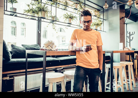 Young male indian freelancer in fast food cafe, handsome man reading text message during work on mobile phone in comfortable coffee shop. Panoramic wi Stock Photo