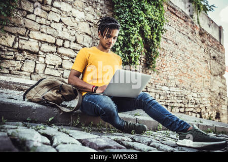 Young slylish man work in laptop outdoors. The concept of study, freelancing, work, technology. Stock Photo