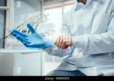 Close up view of male doctor's hands putting on blue sterilized surgical gloves in the medical clinic. Stock Photo