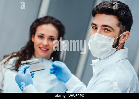 Dentist checking and selecting color of young woman's teeth looking at the camera close up view. selective focus. Stock Photo