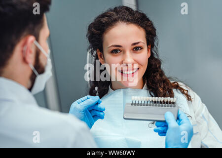 Choice of tooth color with a special scale. Dentist select a shade of tooth enamel for the young pretty girl of the patient. Bleaching, prosthetics, o Stock Photo