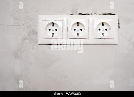 Electric EU socket outlet on gray concrete wall background. Repair in an apartment or in office, replacement of electrical wiring. Close up view. Stock Photo